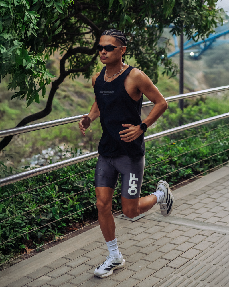 Person running outdoors on a paved path with greenery in the background wearing OFF RUNNING singlet with OFF RUNNING half tights